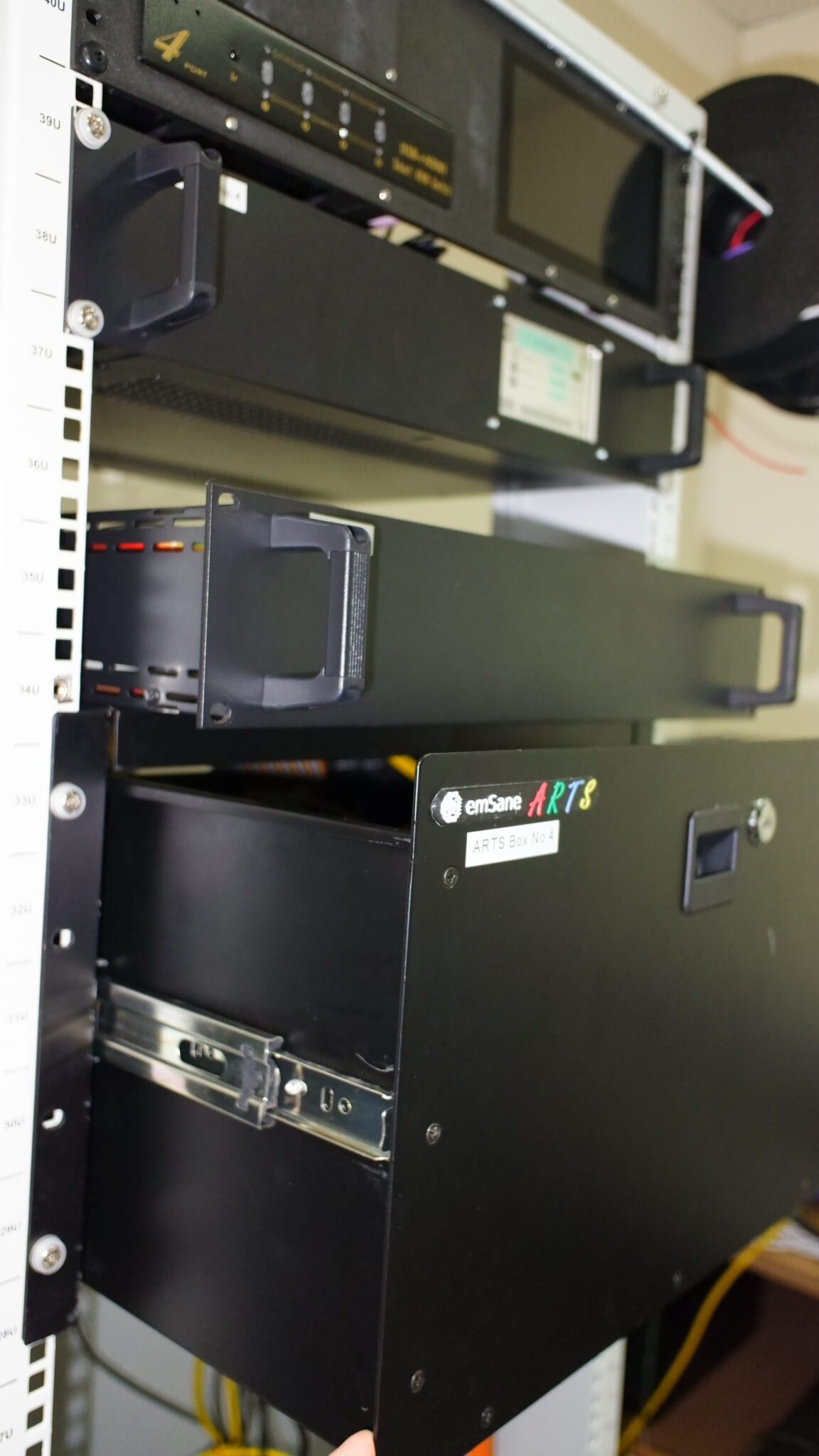 An emSane ARTS Box module pulled out on rails within a customer's server rack, showing internal cabling and connectors.